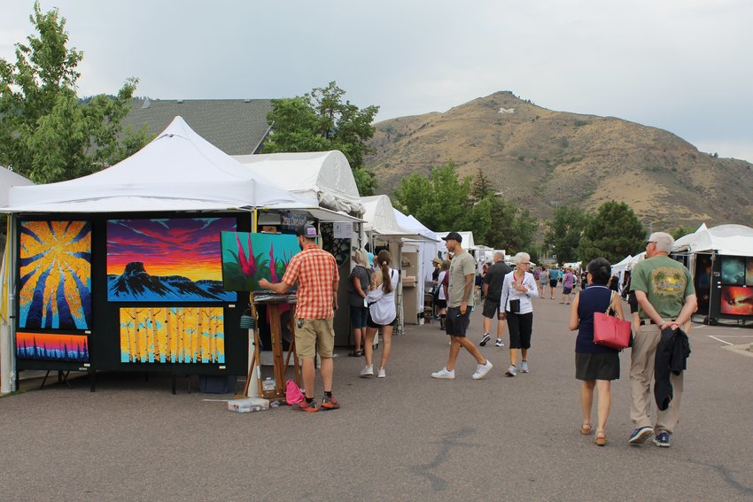 At left, Golden-based painter Jesse Crock hosts his booth as Golden Fine Arts Festival attendees walk along 11th Street Aug. 20.